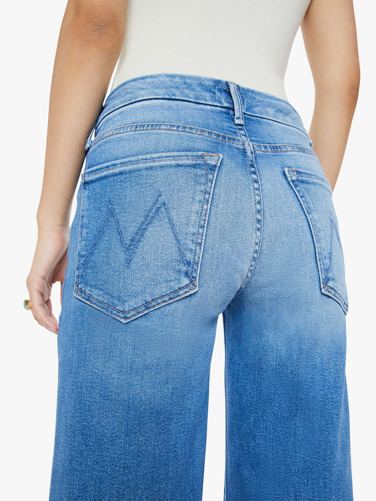 Close up  view of a woman in a mid blue high waisted wide leg jean with a 29-inch inseam and a frayed hem.