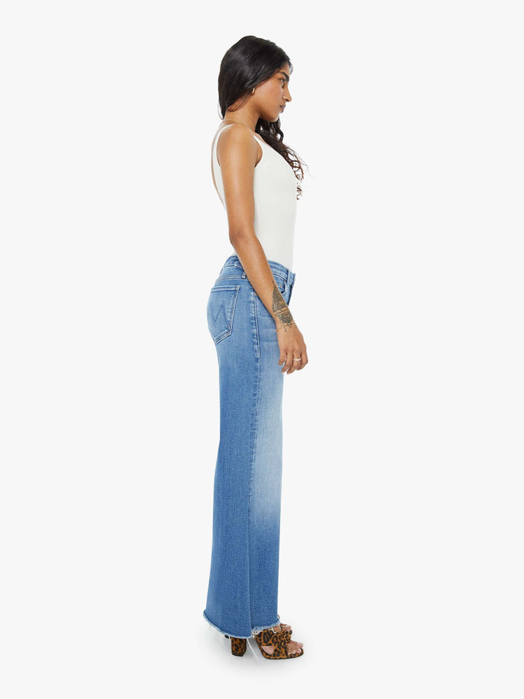 Side view of a petite woman in a high-waisted wide leg has a 31-inch inseam and a frayed hem mid blue jean.