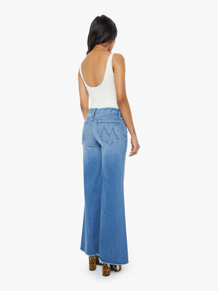 Back view of a petite woman in a high-waisted wide leg has a 31-inch inseam and a frayed hem mid blue jean.