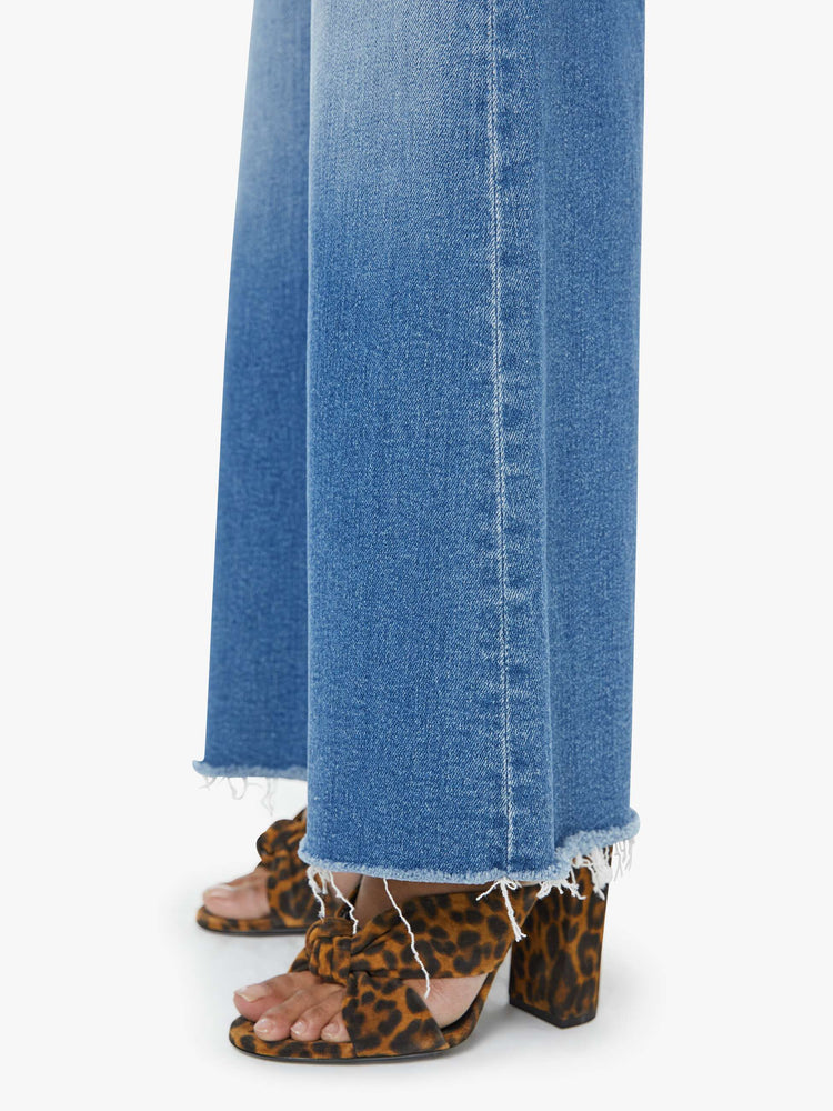 Close up view of a petite woman in a high-waisted wide leg has a 31-inch inseam and a frayed hem mid blue jean.