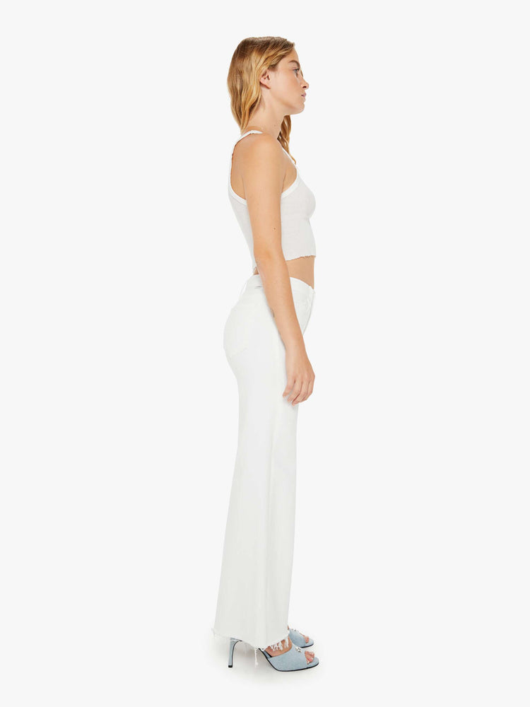 Side view of a woman petite white denim high-waisted wide leg has a full-length inseam and a frayed hem.