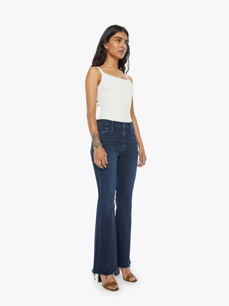 Side angle  view of a dark blue mid-rise flare has a 29-inch inseam with a frayed hem.