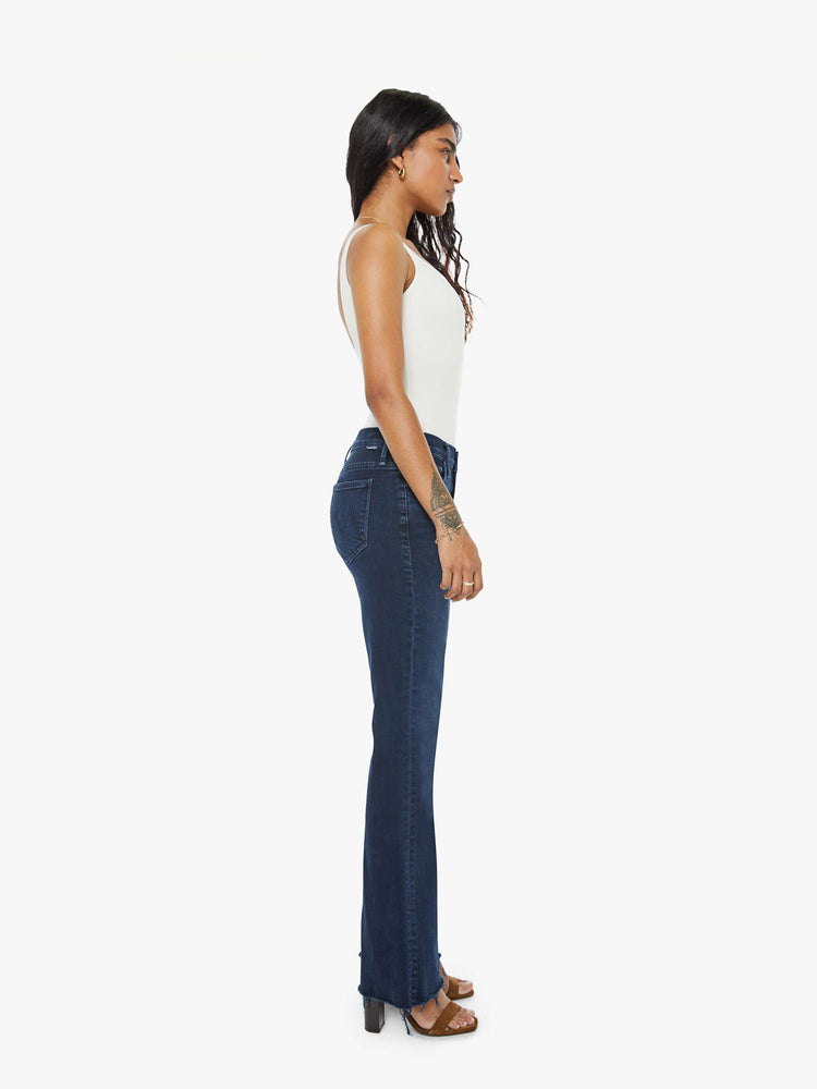 Side view of a dark blue mid-rise flare has a 29-inch inseam with a frayed hem.