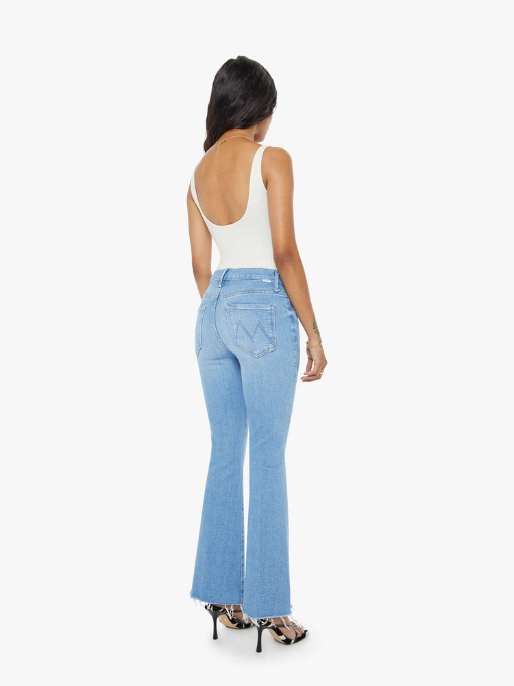 Back view of a petite woman in a light blue mid-rise flare has a zip fly, 28-inch inseam and a frayed hem. 