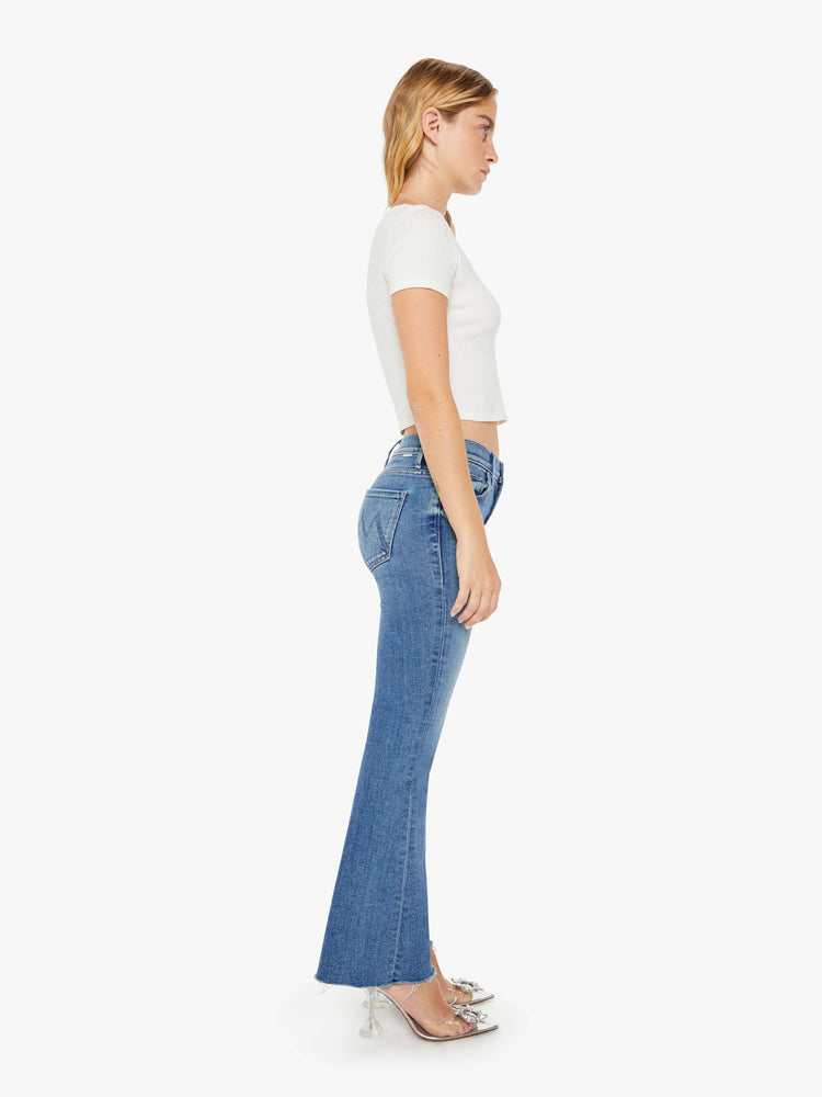 Side view of a petite womans flare jean has a mid rise with a sneaker-length inseam and a frayed hem in a medium blue wash.