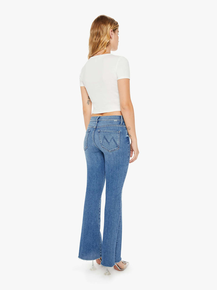 Back view of a petite womans flare jean has a mid rise with a sneaker-length inseam and a frayed hem in a medium blue wash.