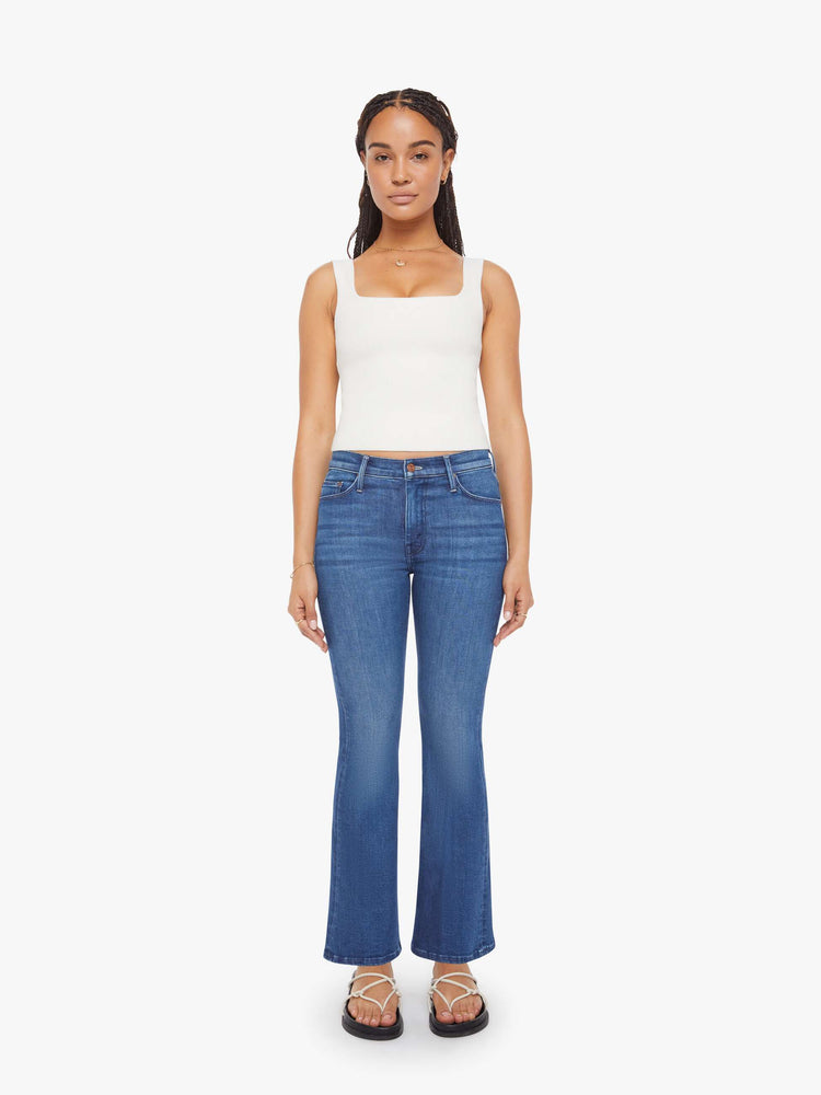 Front view of a petite woman in a med blue flare jean has a mid rise, zip fly, sneaker-length inseam and a clean hem.