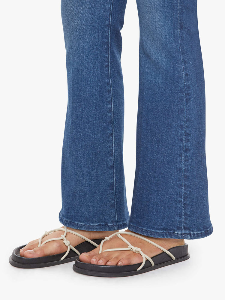 Hem view of a petite woman in a med blue flare jean has a mid rise, zip fly, sneaker-length inseam and a clean hem.