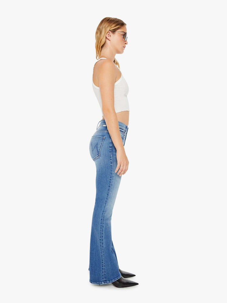 Side view of a petite woman flare jean has a mid rise with a sneaker-length inseam and a clean hem in mid-blue wash.