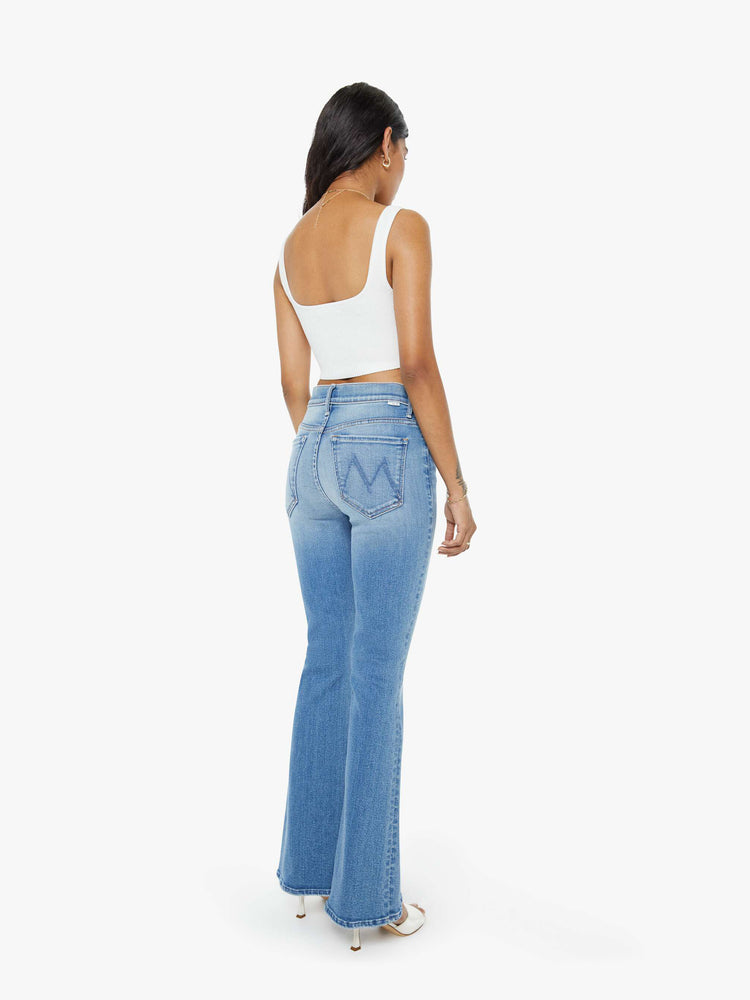 Back view of a petite woman flare jean has a mid rise with a sneaker-length inseam and a clean hem in mid-blue wash.
