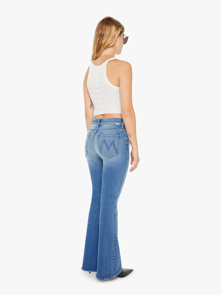 Back view of a petite woman flare jean has a mid rise with a sneaker-length inseam and a clean hem in mid-blue wash.