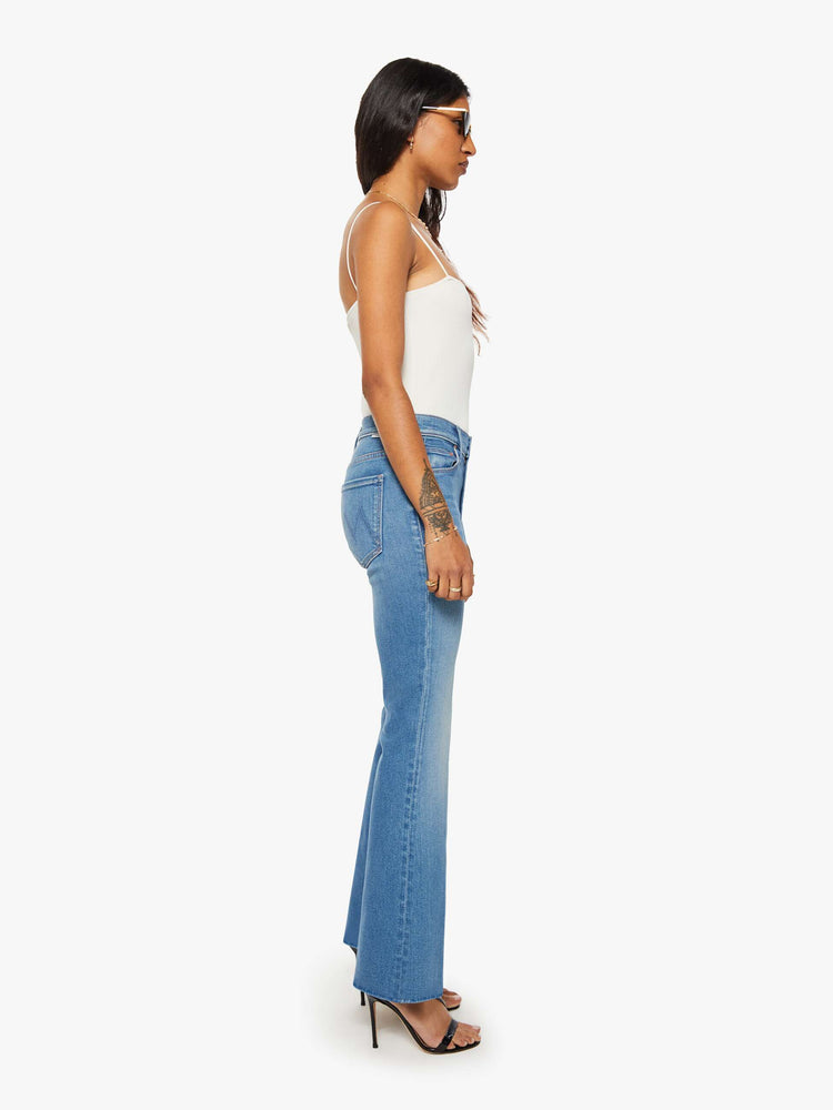 Side view of a petite woman in a mid blue mid rise with a 28-inch inseam and a clean hem.