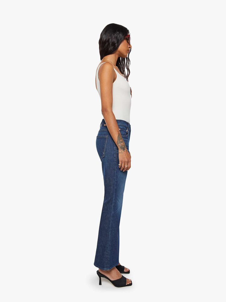 Side view of a woman in a dark blue flare jean has a mid rise with a 28-inch inseam and a clean hem.