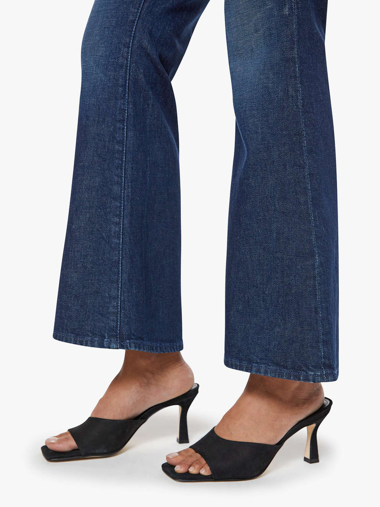 Close up view of a woman in a dark blue flare jean has a mid rise with a 28-inch inseam and a clean hem.