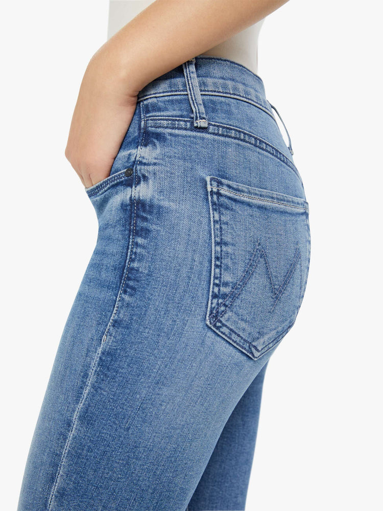 Side close up view of a womens medium blue wash jean featuring a mid rise.