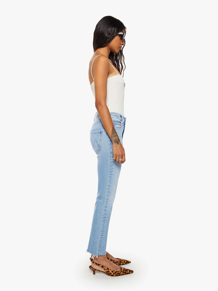 Side view of a petites woman in a mid-rise straight leg hits at the ankle with a frayed hem in a medium blue 