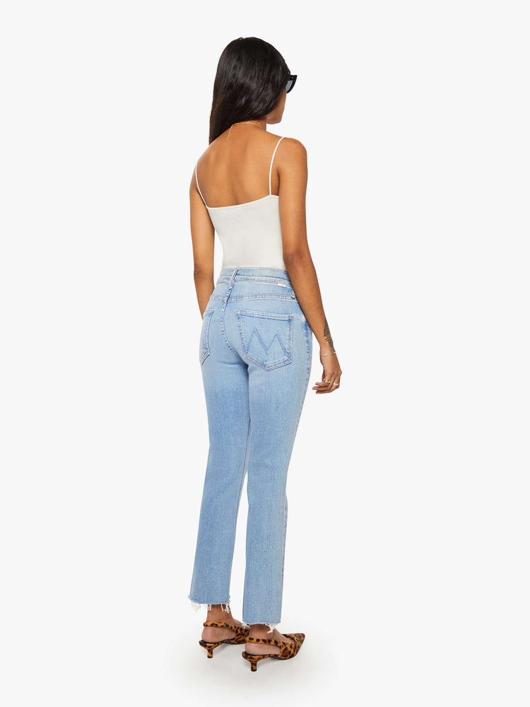 Back view of a petites woman in a mid-rise straight leg hits at the ankle with a frayed hem in a medium blue wash.