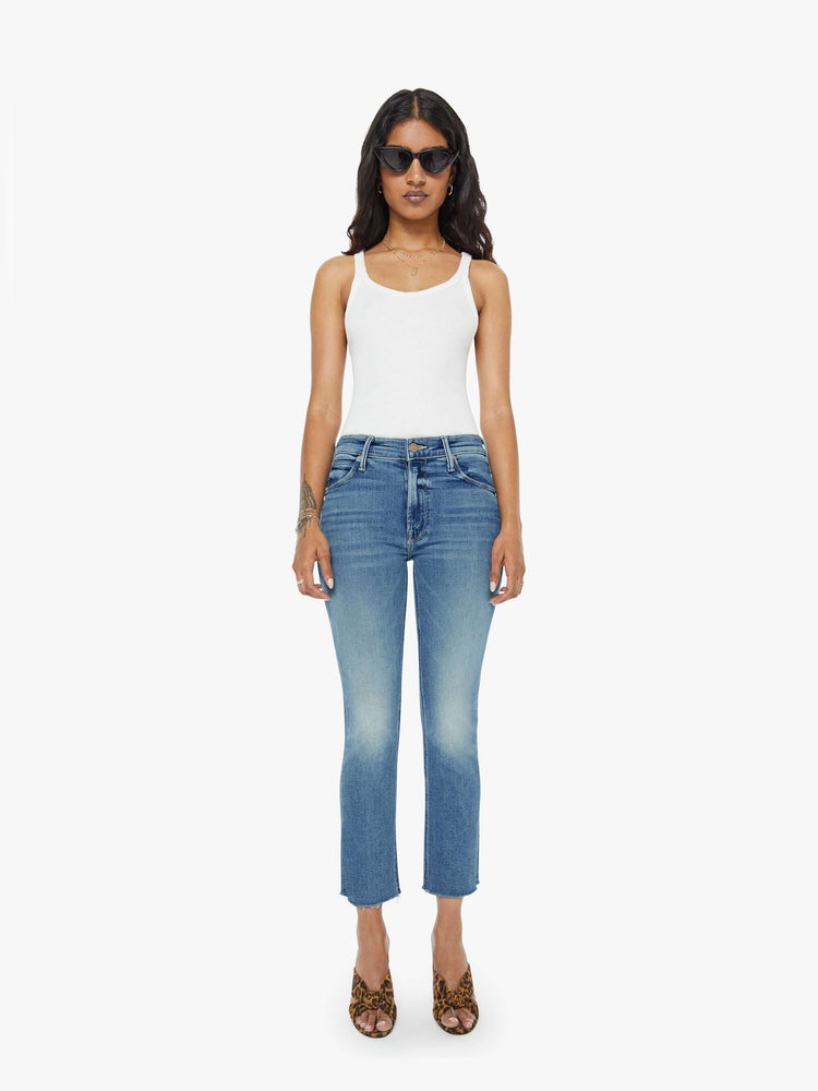 Front view of a womens mid rise jean in a medium blue wash, featuring an ankle fray.