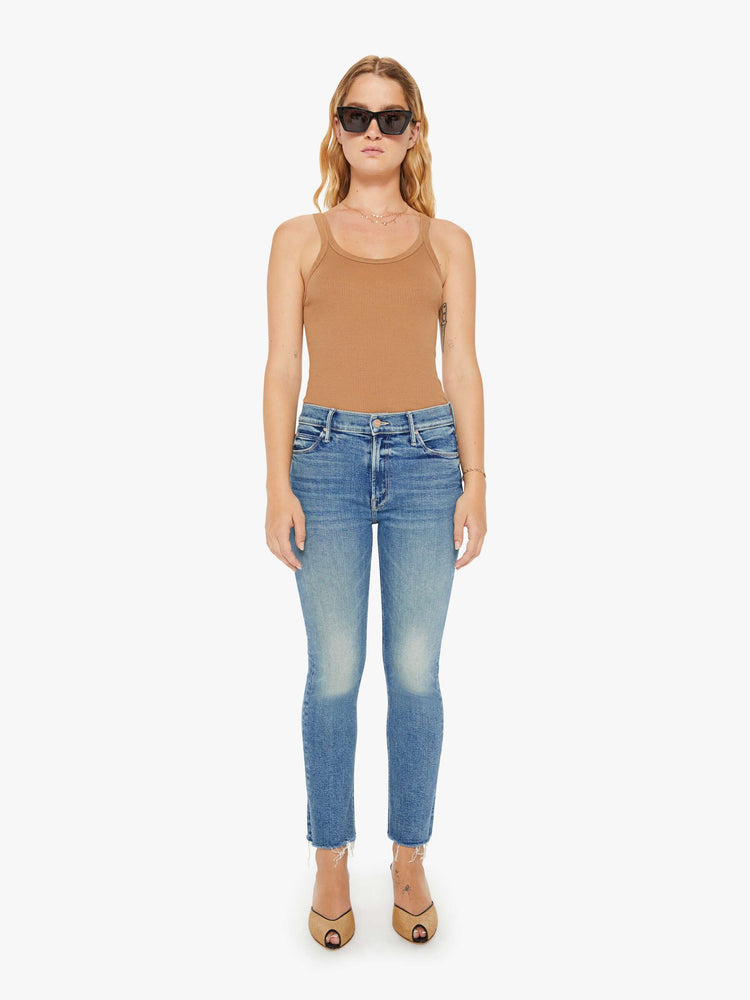 Front view of a womens mid rise jean in a medium blue wash, featuring an ankle fray.