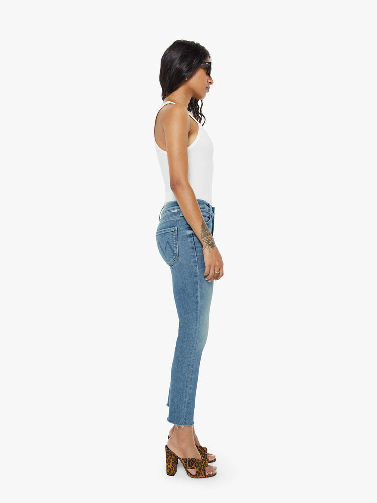 Side view of a womens mid rise jean in a medium blue wash, featuring an ankle fray.