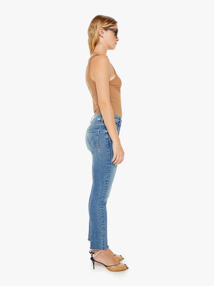 Side view of a womens mid rise jean in a medium blue wash, featuring an ankle fray.