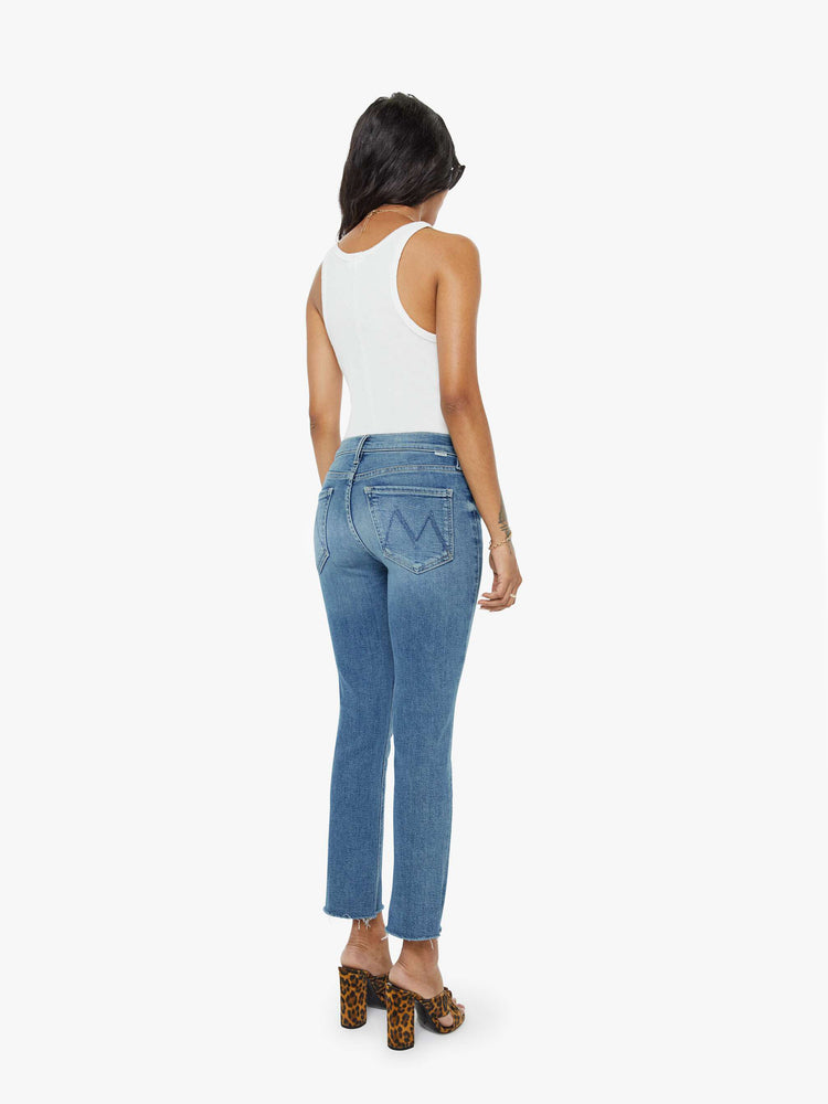 Back view of a womens mid rise jean in a medium blue wash, featuring an ankle fray.