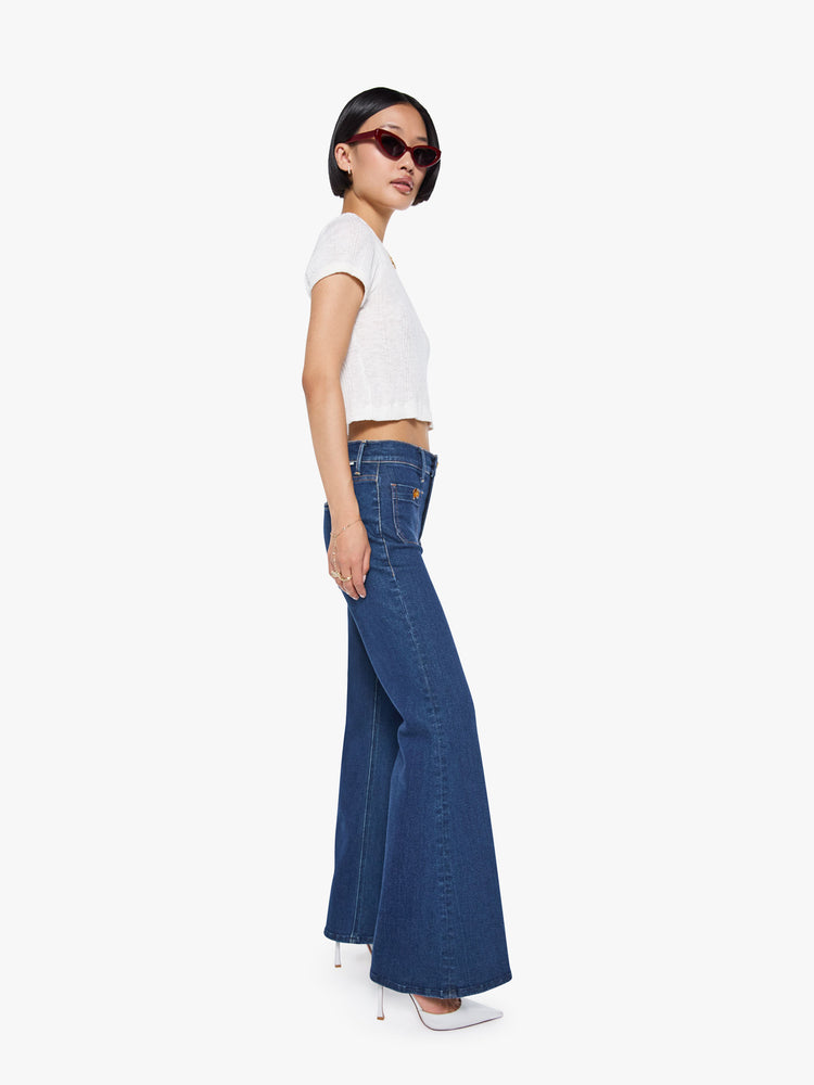 Side view of a high rise dark blue denim flare jeans with front patch pockets.