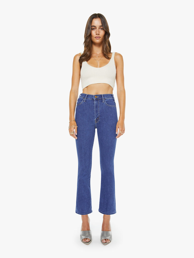 Front view of a woman in a midblue  high-rise flare has an ankle-length inseam, zip fly and a clean hem. 