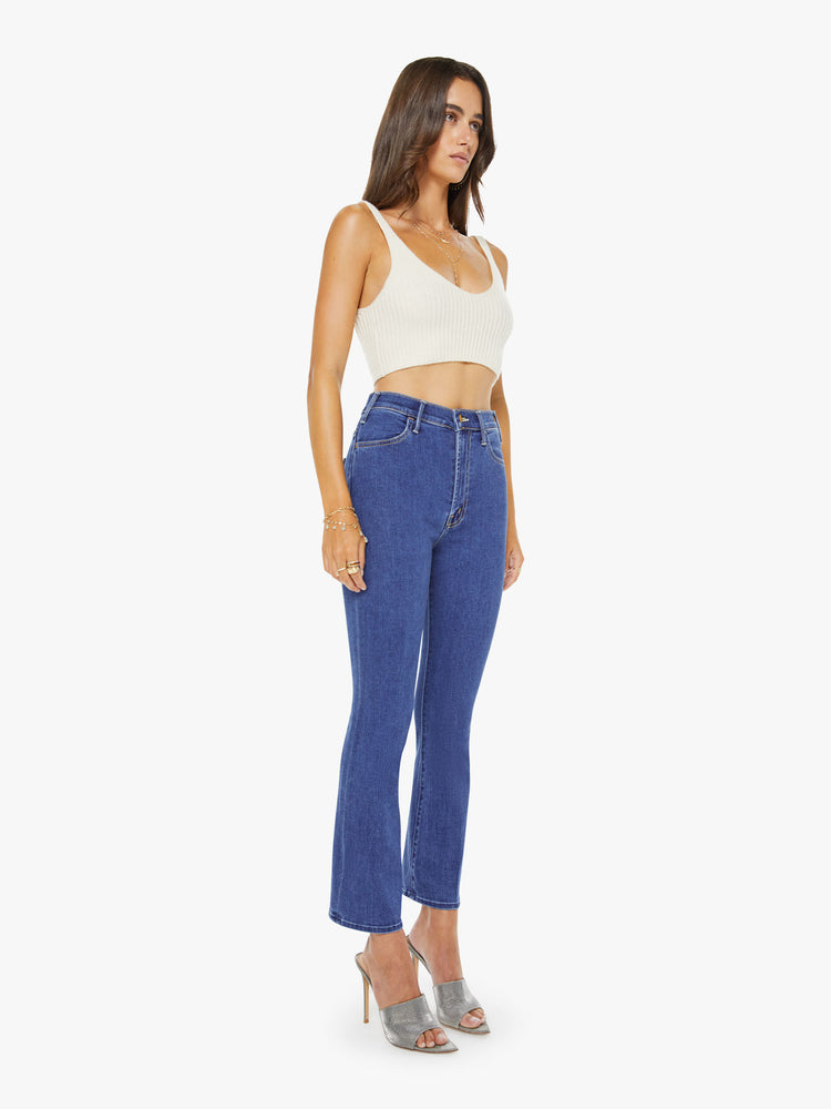 Side angle view of a woman in a midblue  high-rise flare has an ankle-length inseam, zip fly and a clean hem.