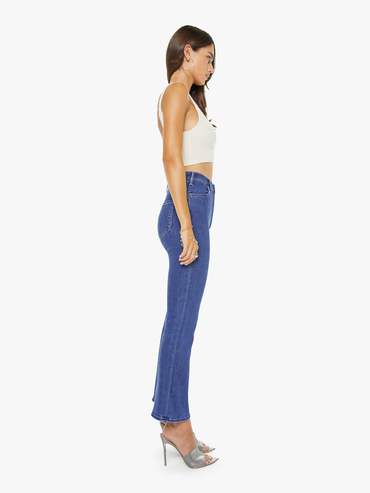 Back view of a woman in a midblue  high-rise flare has an ankle-length inseam, zip fly and a clean hem.