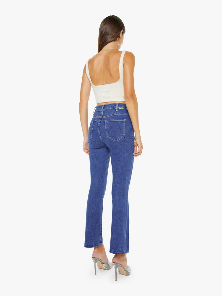 Back view of a woman in a midblue  high-rise flare has an ankle-length inseam, zip fly and a clean hem.