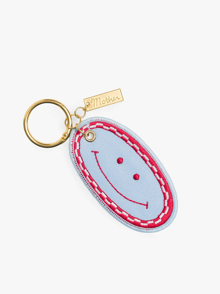 Flat view baby blue, red and white, the keychain features an embroidered patch with MOTHER's name on one side and a smiley face on the other.