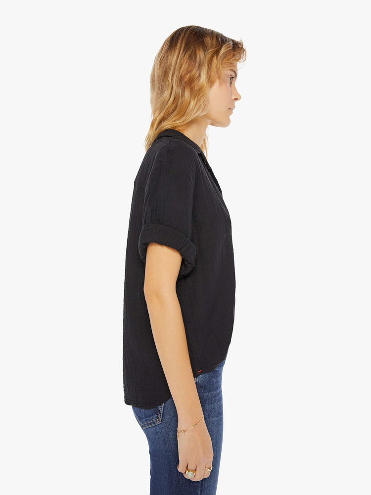 Womens side view of a collared, black, V-neck shirt with rolled elbow-length sleeves and a slightly boxy fit.