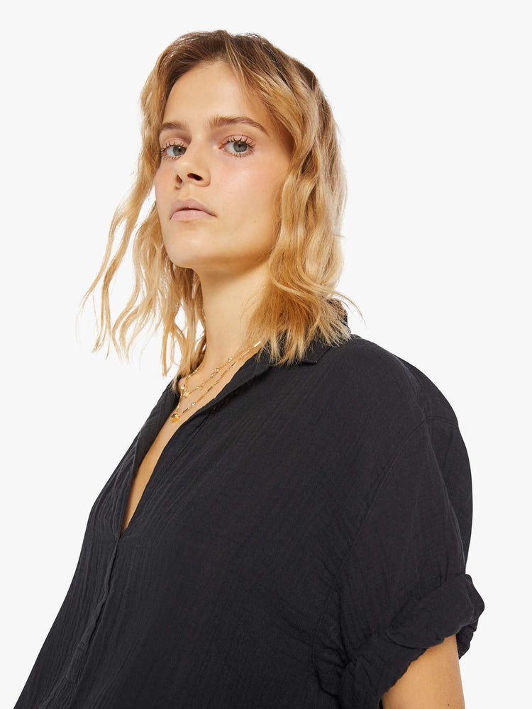 Womens detailed view of a collared, black, V-neck shirt with rolled elbow-length sleeves and a slightly boxy fit.