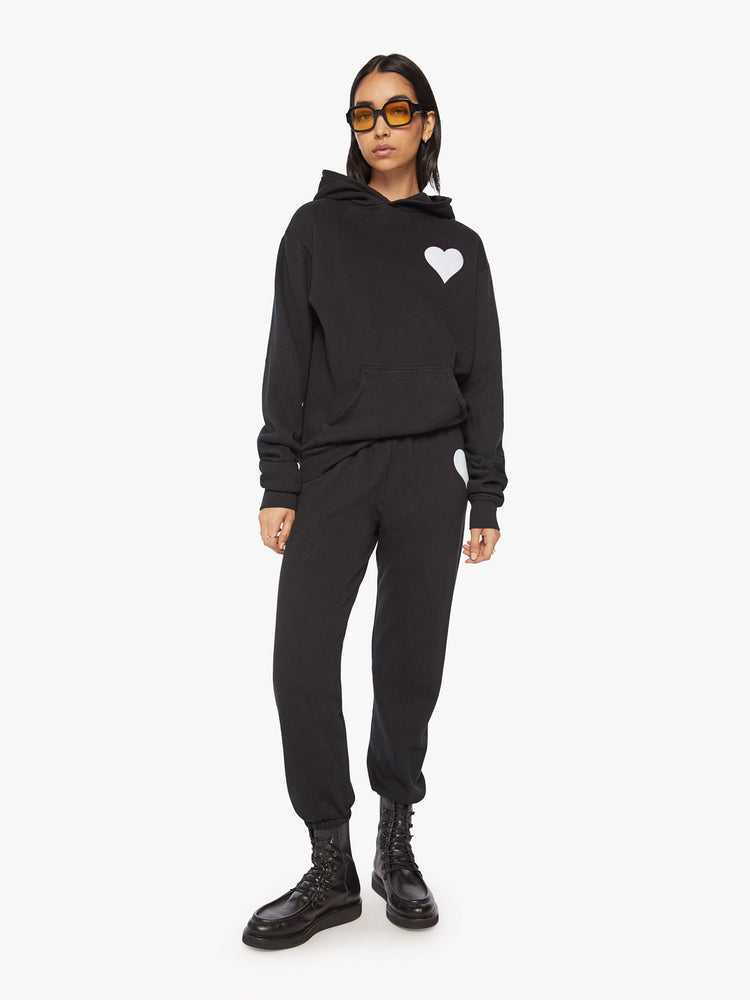 Front full body view of a Womens black hoodie pullover with a front kangaroo pocket and a white heart graphic printed on the chest.