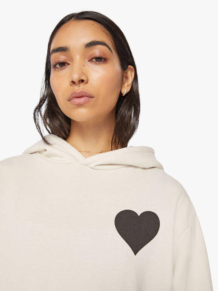 Close up view of a Womens white hoodie pullover with a front kangaroo pocket and a black heart graphic printed on the chest.