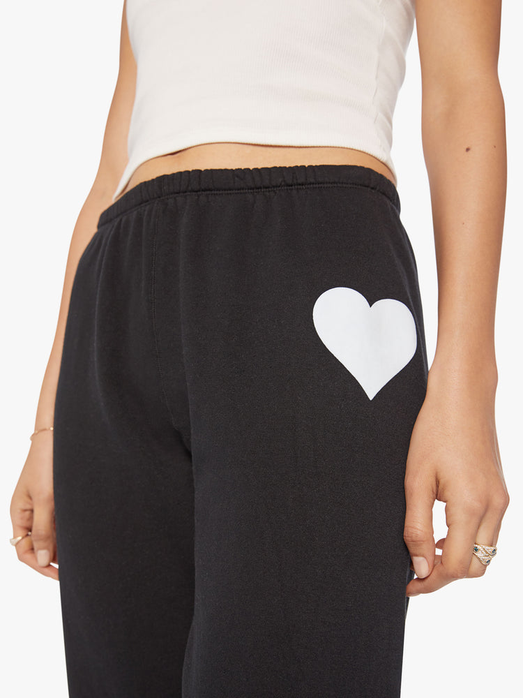 Close up view of a white heart graphic, printed on a pair of black sweatpants.