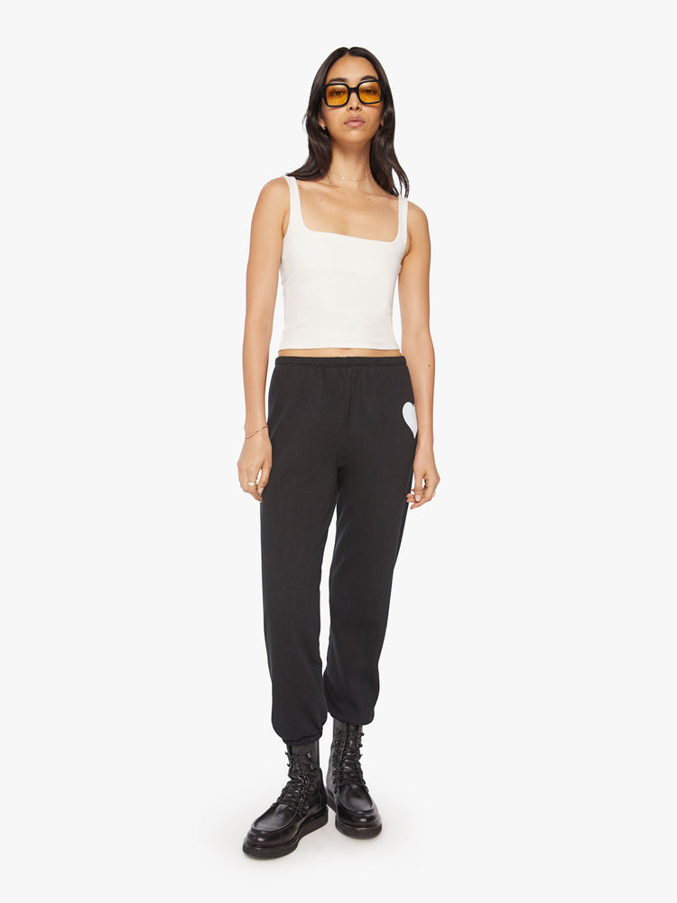 Full body front view of a Womens black sweatpant with a white heart graphic printed on the left side hip.