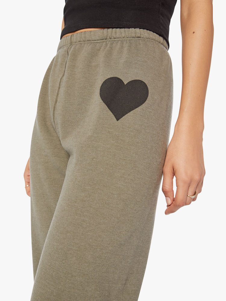 Detail view of a woman army green sweatpants with a black heart on the hip have an elastic waist and cuffs for a loose, comfortable fit.