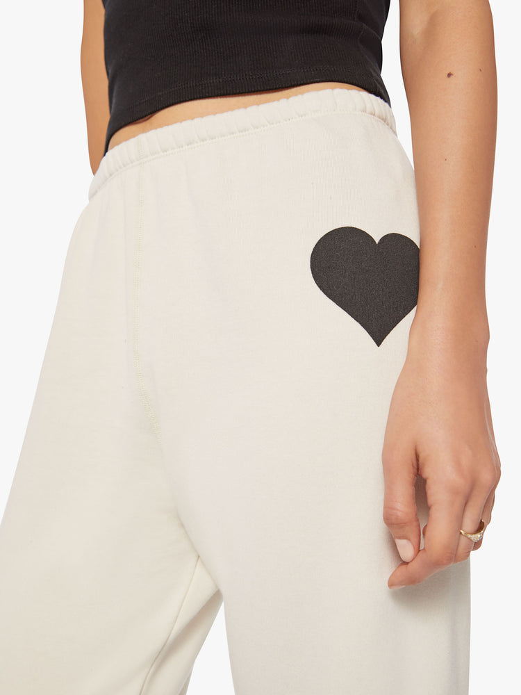 Close up view of a Womens white sweatpant with a black heart graphic printed on the left side hip.