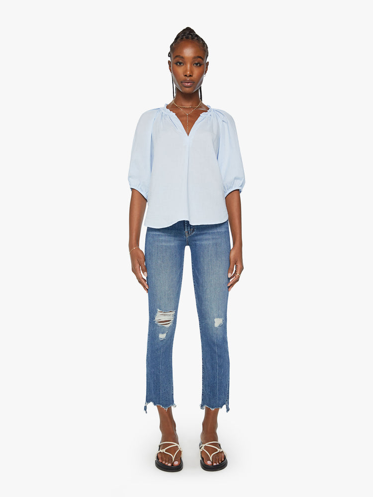 Full body view of view of woman light blue hue blouse features a ruffled collar with a deep V-neck, elbow-length balloon sleeves and a loose fit.