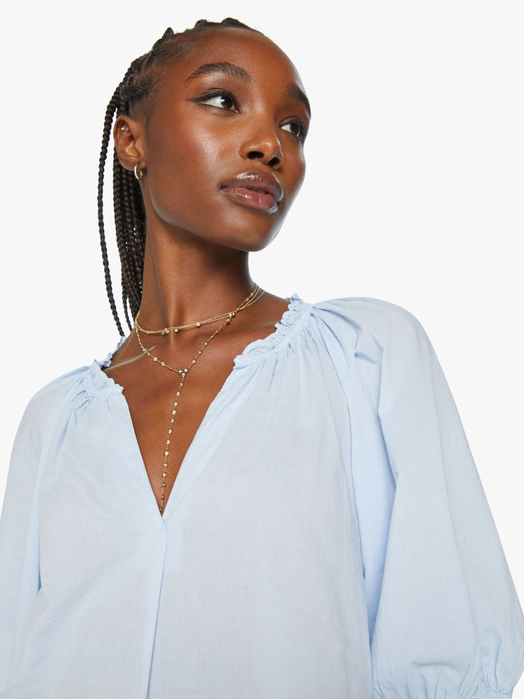 Close up view of woman light blue hue blouse features a ruffled collar with a deep V-neck, elbow-length balloon sleeves and a loose fit.