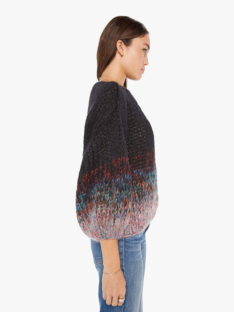 Side view of a womens chunky knit sweater featuring a black to multi color gradient and billow sleeves.