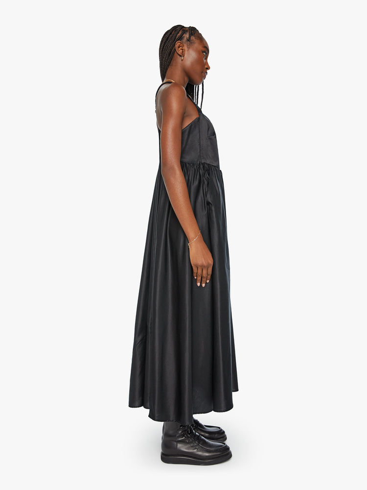 Side view of a woman faded black hue dress and features a square neck with extra long straps, front pockets, a gathered waist and an ankle-length hem.