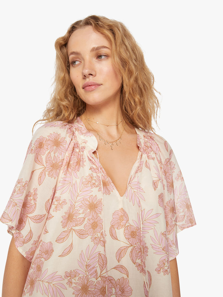 Close up view of a woman's dress designed with a keyhole neckline and flowy short sleeves in a pink and orange floral pattern.
