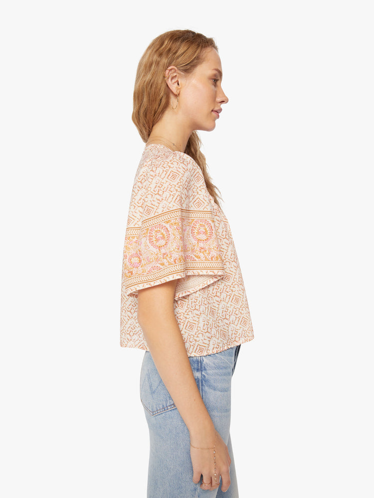 Side view of a woman pink pattern blouse is designed with a V-neck, short, boxy sleeves and slight cropped hem.