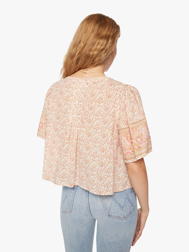 Back view of a woman pink pattern blouse is designed with a V-neck, short, boxy sleeves and slight cropped hem.