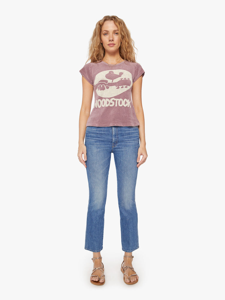 Full body view of a woman of a dark purple tee honors the Woodstock Music and Art Fair made famous in the 1960s with a faded white graphic on the front.