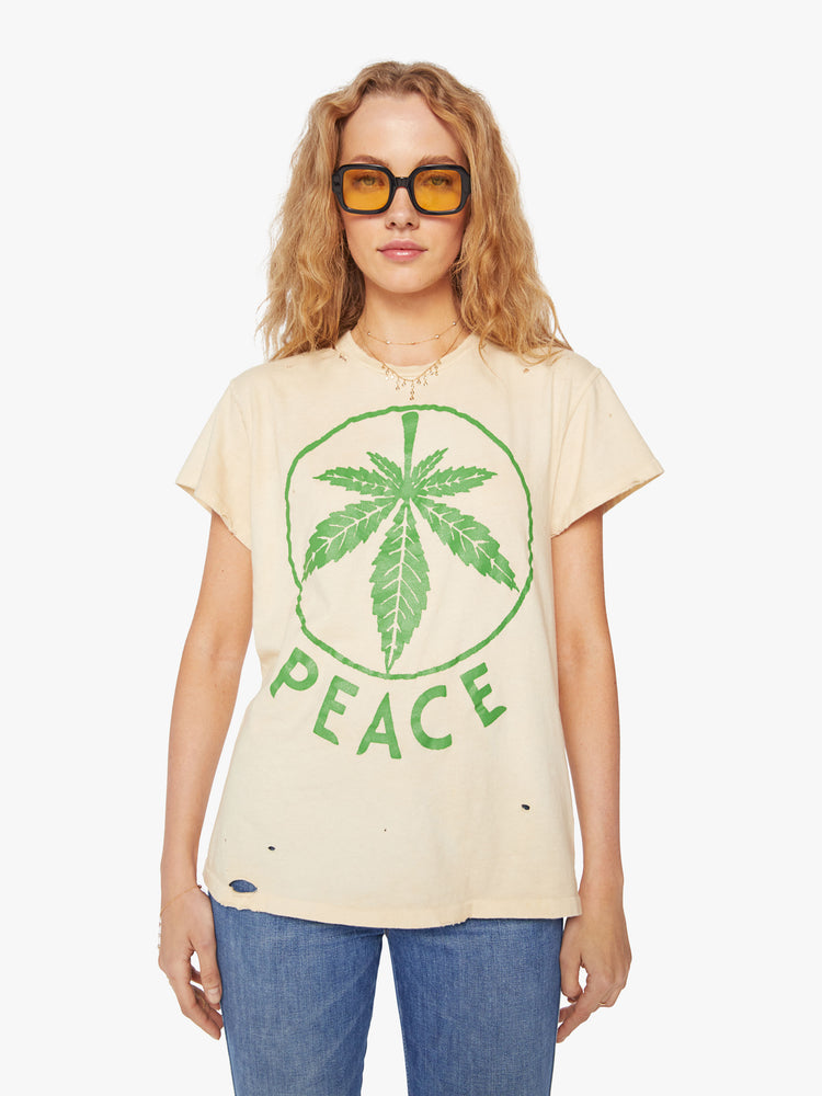 WOMEN Front view of a woman tea-stained white hue with small tears throughout, the tee offers a sign of peace with a green weed leaf graphic on the front.