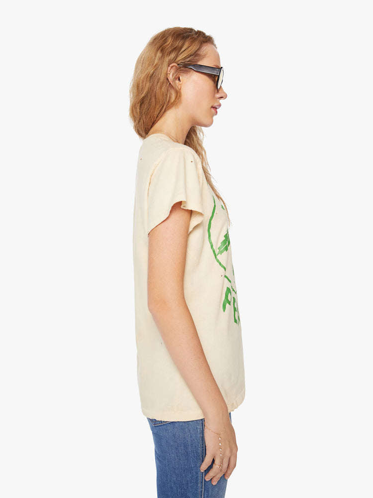 WOMEN Side view of a woman tea-stained white hue with small tears throughout, the tee offers a sign of peace with a green weed leaf graphic on the front.